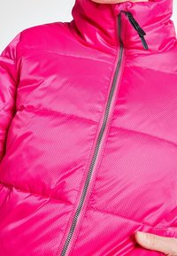 Doudoune fuchsia avec col montant, texture brillante, motif matelassé horizontal, fermeture éclair complète et quincaillerie argentée contrastante.