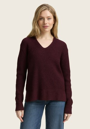 Burgunderfarbener strukturiertes Strickpullover mit V-Ausschnitt und langen Ärmeln, mit geripptem Saum und Bündchen. Kombiniert mit blauen Jeans.