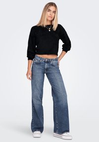 Black fuzzy cropped sweater, blue wide-leg jeans, and white sneakers. The jeans have a faded wash and raw hem detailing.
