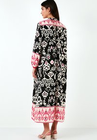 Black and white patterned long dress with pink accents, featuring a round neckline and long sleeves, made from lightweight fabric.