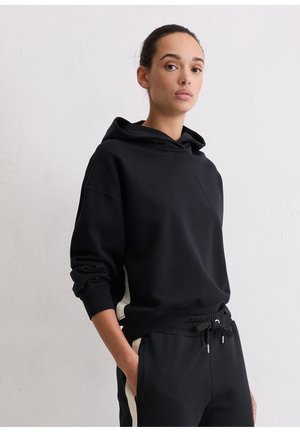 Black hoodie with a relaxed fit, featuring a drawstring hood, ribbed cuffs, and cream side accents. Paired with matching black joggers.