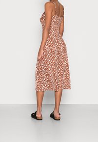 Vestido marrón con estampado floral en blanco, de largo midi, con tirantes ajustables y un cuerpo ajustado. Lleva unas sandalias negras con suelas de corcho.