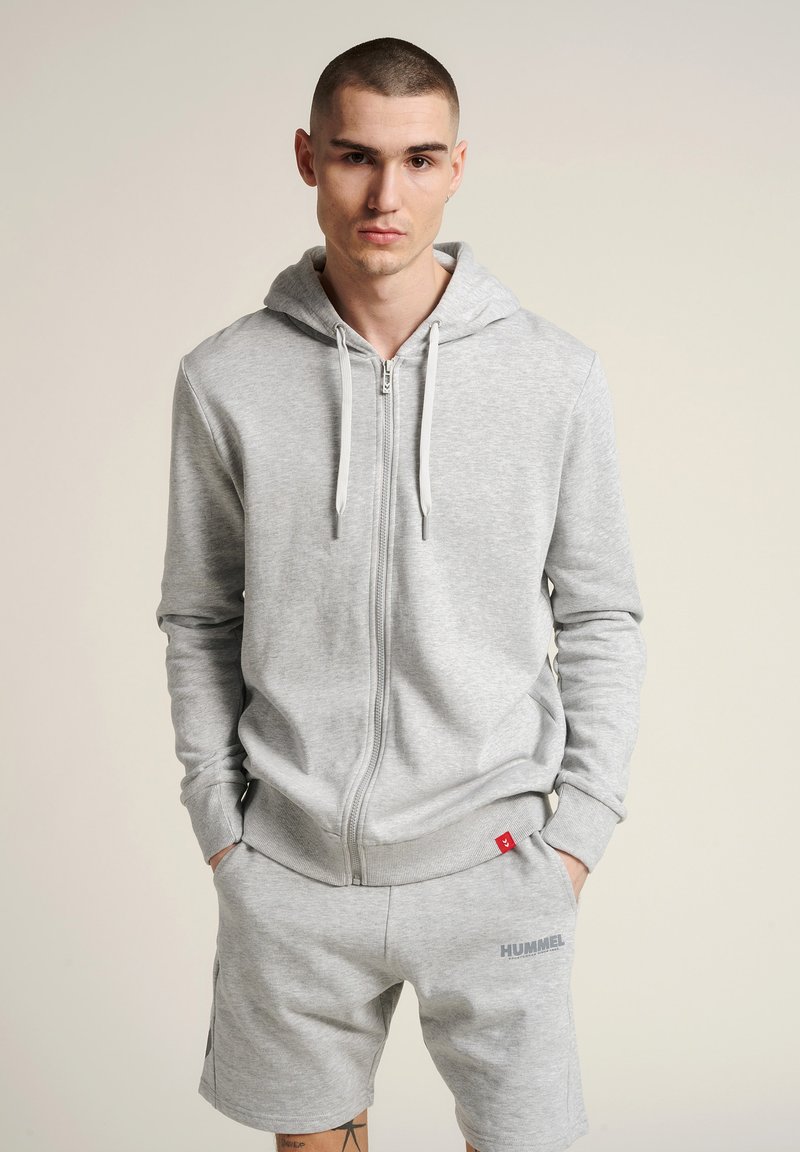 Helles graues Zip-Hoodie mit einer Fronttasche, verstellbarem Kordelzug und gerippten Bündchen. Kombiniert mit passenden Shorts mit Logo-Details.