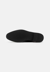Semelle de chaussure noire avec une surface lisse et des détails de grip texturés. Dotée d'un bout arrondi et d'un talon légèrement surélevé pour la stabilité.