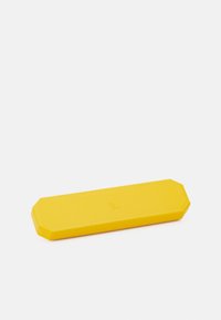 Caso octagonal amarillo, hecho de material texturizado, con un sutil logo grabado en el centro. Diseño robusto y compacto.