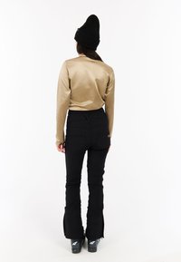 Gouden longsleeve top gecombineerd met zwarte aansluitende broek met ritssluitingen aan de onderkant, gedragen met zwarte skischoenen, en afgewerkt met een zwarte gebreide beanie.