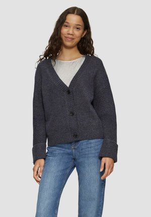 Dunkelgrauer Cardigan mit tiefem V-Ausschnitt, gerippter Textur und vier Knöpfen. Mit weiten Ärmeln und lockerer Passform, kombiniert mit hellblauen Jeans.