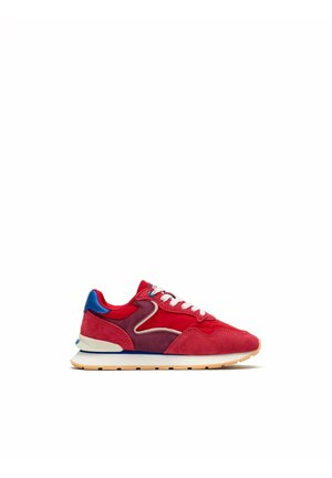 Zapatilla deportiva de ante y tela roja y púrpura con cordones blancos, detalle azul en el talón y suela beige con franja azul.