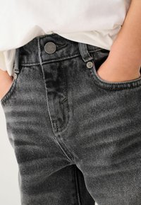 Mörkgrå jeans i denim, med femfickorsdesign, synliga sömmar och metallbeslag vid midjan och fickorna.