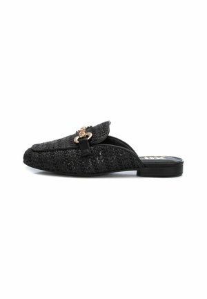 Zapato negro de tela trenzada tipo slip-on con punta redondeada, con un acento de cadena de tono dorado y un tacón negro bajo. Superficie texturizada con un brillo sutil.