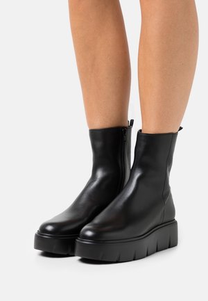 Bottines en cuir noir avec une finition lisse, fermeture à glissière sur le côté et une semelle plateforme épaisse avec des rainures verticales.