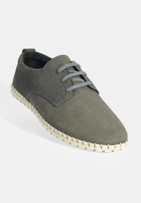 Chaussure en cuir perforé vert avec des lacets gris et une surface texturée, dotée d'une semelle tissée couleur crème pour plus de détails.