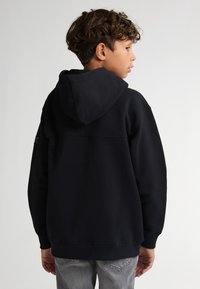 Hoodie noir avec capuche à cordon, présentant un design uni et des poignets côtelés. La vue arrière montre une construction sans coutures avec une coupe décontractée.