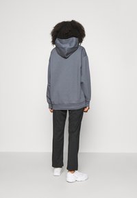 Sweat à capuche gris avec une coupe décontractée, associé à un pantalon noir et des baskets blanches, présenté de dos sur un fond neutre.