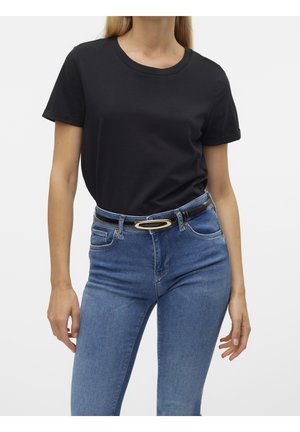 Kobieta ubrana w jednolity czarny t-shirt z krótkim rękawem, włożony do niebieskich dżinsów z czarnym paskiem z złotą owalną klamrą.