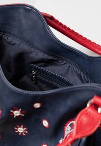 Granatowa torebka z czerwonymi akcentami, zdobiona haftem, o gładkiej fakturze i wewnętrznej kieszeni na zamek dla bezpiecznego przechowywania.