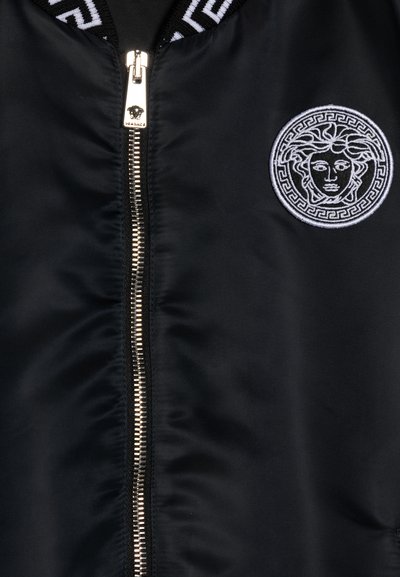 Black bomber jacket made of nylon, featuring a silver zipper and a white embroidered logo within a circular design. Striped ribbed collar.