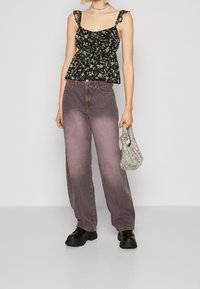 Svart blommig peplumtop med ryschade band, kombinerad med ljuslila vida jeans. Accessoarer inkluderar en silver nätväska och kraftiga kängor.