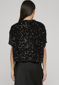 Sort cropped top lavet af paliettemateriale, med en afslappet pasform og korte ærmer, med en tekstureret overflade og skinnende detaljer.