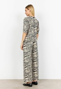 Beige and black zebra-striped co-ord set made of soft fabric; loose-fitting top with three-quarter sleeves, wide-leg pants, and flat shoes.