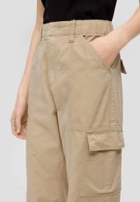 Beige cargobroek van katoen, met zijzakken, een elastische tailleband en een patchzak op het been. Gladde textuur, slim fit.