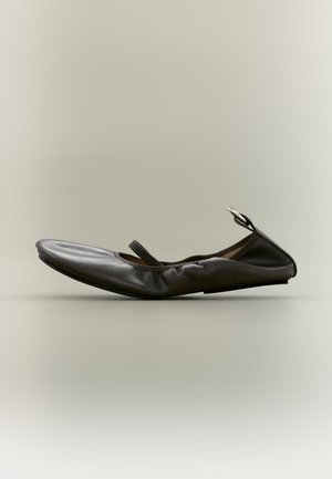 Chaussure plate Mary Jane en cuir foncé, à bout pointu, bride fine et boucle argentée, représentée de profil sur un fond uni.