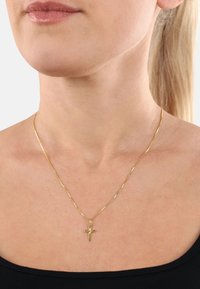 Collana in oro con un piccolo pendente a croce, texture liscia, design snello, appoggiata su un collo nudo.