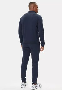 Tuta blu navy in morbido materiale, con collo zip, polsini a coste e pantaloni aderenti abbinati dal design elegante.