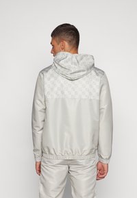 Chaqueta gris claro con un respaldo texturizado, dobladillo elástico y capucha. Material suave con un diseño contemporáneo.