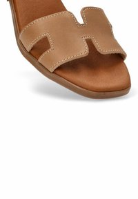 Sandalia deslizante de cuero marrón con diseño abierto en la punta y cortes, y costuras en contraste en las correas. Plantilla suave con superficie texturizada.