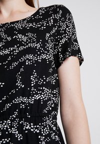 Svart klänning med vitt abstrakt mönster, korta ärmar, rund halsringning och rynkad midja. Mjuk tygkänsla med detaljer i elastisk midja.