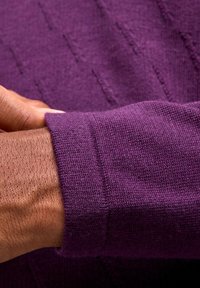 Paarse gebreide trui met een geribbelde manchet. De textuur ziet er zacht uit met zichtbare stikpatronen, wat zorgt voor een strakke pasvorm rond de pols.