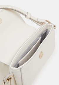 Sac à main en cuir blanc avec une texture lisse, doté d'une seule bandoulière, d'une fermeture à pression et d'un intérieur gris avec des fentes pour cartes.