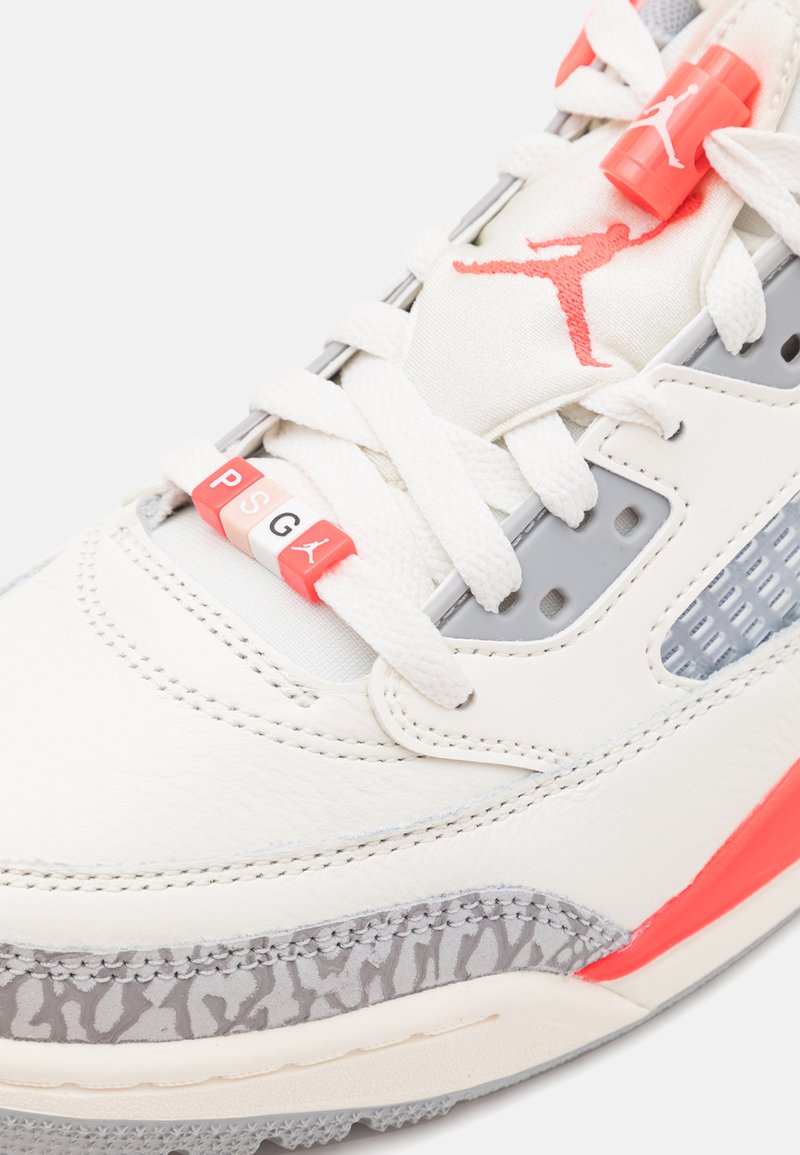 Weiße Leder-Sneaker mit grauen Akzenten, einer gemusterten Zwischensohle und korallenfarbenen Details. Enthält einen markierten Schnürzug und perforierte Abschnitte.