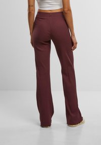 Pantalons côtelés bordeaux avec une forme évasée, une taille élastique et une texture douce, présentant un motif vertical subtil.