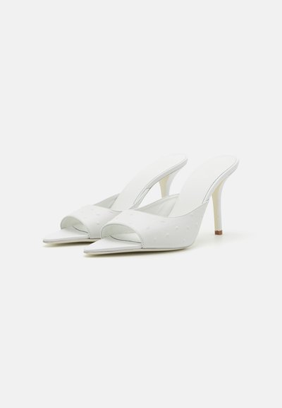 Zapatos de tacón abierto en color blanco con una superficie texturizada que presenta pequeños puntos y un tacón alto y delgado.