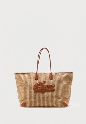 Grande borsa a mano beige intrecciata con manici in pelle marrone e un emblema frontale in pelle marrone a motivo coccodrillo.