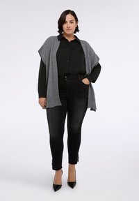 Cardigan de punto gris sobre una camisa negra con botones, combinado con jeans ajustados negros y tacones de punta negra. Texturas suaves, ajuste informal.