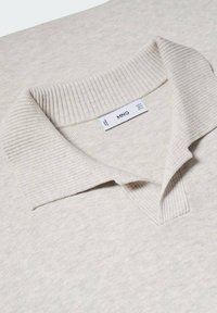 Polo shirt beige clair avec un col et une patte de boutonnage côtelés. Le tissu a une texture douce avec des variations subtiles. Étiquette "MNG" visible à l'intérieur.