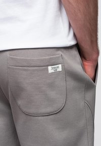 Grå joggers i mjukt material med en bakficka med en etikett och synliga sömdetaljer. Midjan är elastisk för extra komfort.