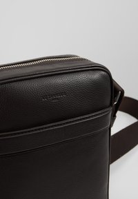 Borsa a tracolla in pelle marrone con finitura testurizzata, dotata di cerniera argentata, tracolla regolabile e logo impresso.