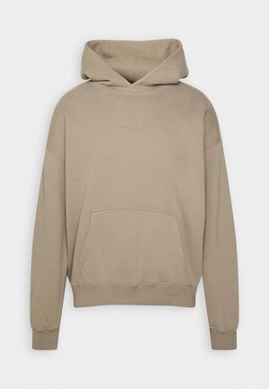 Beżowa bluza z kapturem, kangurzą kieszenią, długimi rękawami i subtelnym, małym napisem na środku klatki piersiowej.