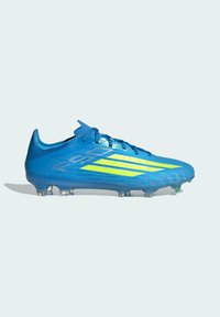 Chaussure de football bleue avec des bandes jaunes, design bas et crampons moulés pour jeu sur terrain ferme, montrée en profil latéral sur un fond clair.