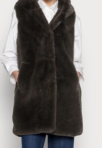 Mörkgrå faux fur-väst med huva, med knäppning och sidofickor, bärs över en vit skjorta och parats med blå jeans.