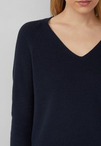 Granatowy sweter z dzianiny z dekoltem w kształcie litery V, prążkowaną teksturą i długimi rękawami. Materiał wydaje się miękki i ma dopasowany krój.