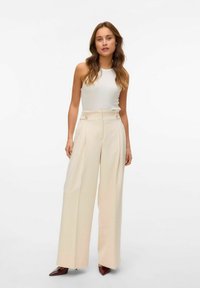 Pantalon large crème à taille haute, avec deux accents de boutons et une texture douce. Assorti à un haut débardeur blanc ajusté.