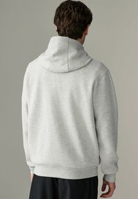 Sudadera gris acanalada con cuello alto y puños elásticos. Textura suave y diseño ajustado. Vista desde atrás, mostrando los detalles de la costura.