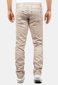 Pantalon en velours côtelé beige avec des rayures verticales, coupe ajustée et deux poches arrière. Associé à des baskets blanches avec des accents noirs.
