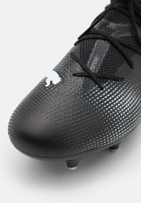 Scarpa da calcio nera con superficie testurizzata e motivo sottile. Presenta lacci neri e un logo bianco prominente sul lato.