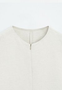 T-shirt blanc à col rond avec une fermeture éclair centrale dans le dos et une couture simple autour de l'encolure.